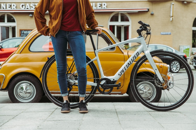 Frau steht mit einem Specialized e-Bike vor einem gelben Auto