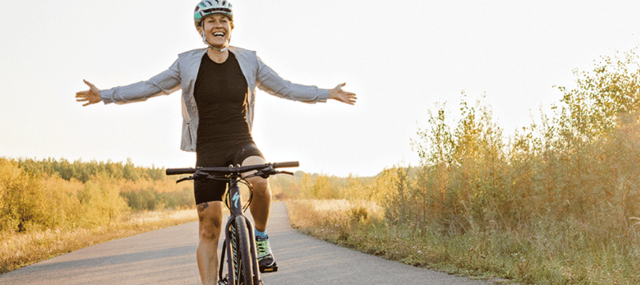 Eine Frau fährt auf einem e-Bike der Marke Specialized ein Feldweg entlang, während sie die Arme ausstreckt und dabei lacht